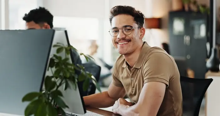 A young adult with autism smiling while working at a computer in a modern office, representing the success of neurodiverse individuals in professional career paths in San Diego.