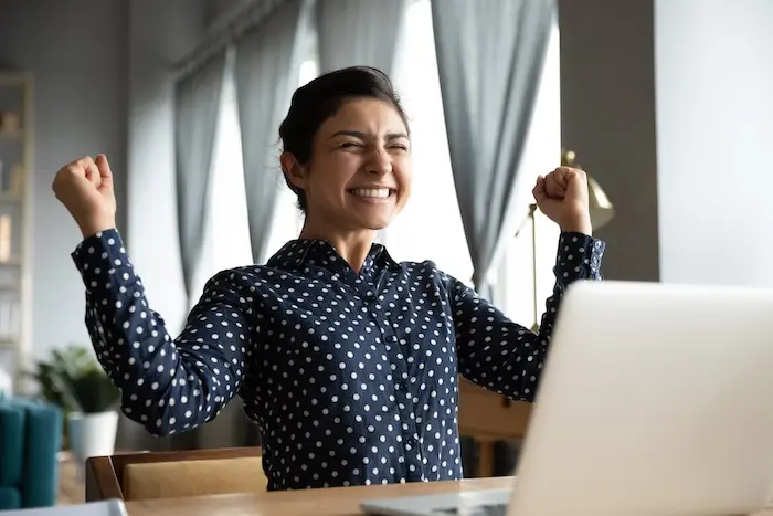 A young woman with autism cheering with excitement at her desk, celebrating a successful job placement or career milestone in San Diego.