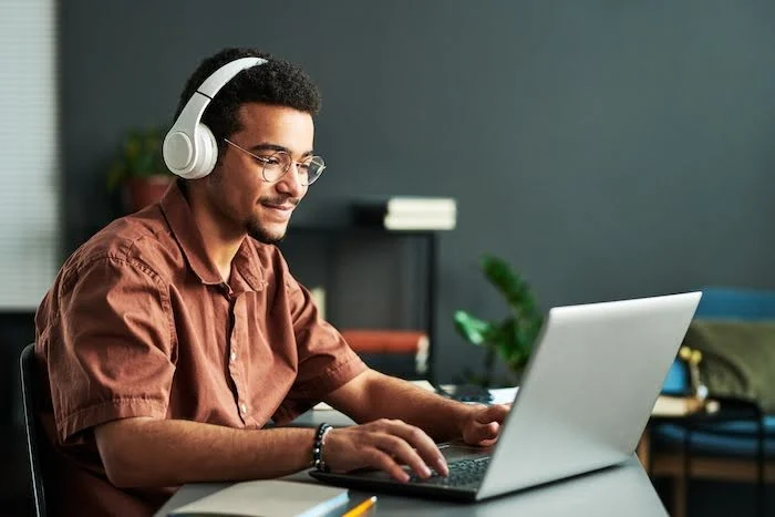 Young Black man wearing headphones and doing research on his laptop.