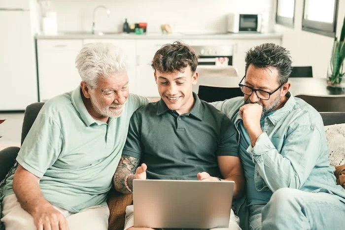 Young Caucasian man showing something to his father and grandfather on his laptop.