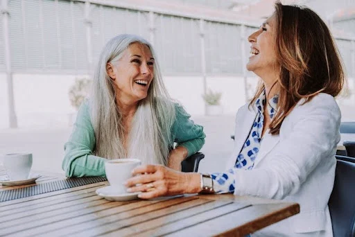 Two senior women laughing and having coffee together.