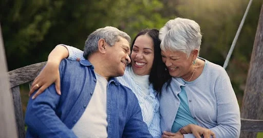 Hispanic parents hugging their adult daughter.