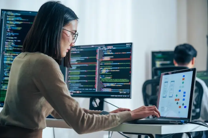 A woman with autism working as a software developer, focused on coding across multiple monitors, highlighting the high-level technical skills and career paths in California's tech industry.