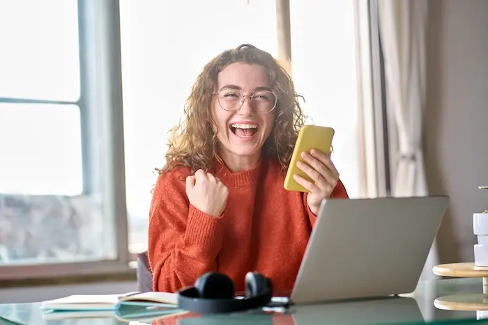 A young woman with autism cheering with excitement while looking at her laptop, celebrating a successful job offer or career milestone in California.